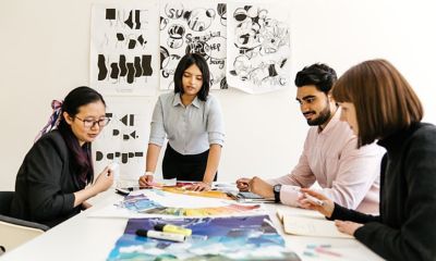 RMIT students gathered around a table of artwork, with posters on the wall behind them.