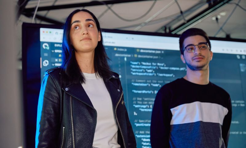Two information technology students standing in front of a screen displaying code