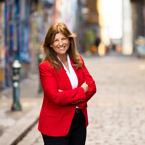 Profile photo of Professor Julie Cogin standing in a laneway and smiling towards the camera with arms crossed. 