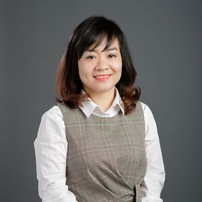 Kate Nguyen profile photo. Kate is sitting in front of a grey wall. Kate is wearing a dress and smiling