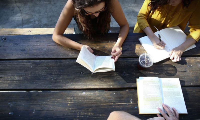 three people sitting at an outdoor table studying notes and textbooks