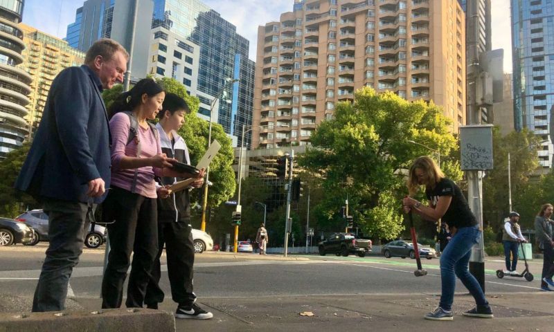 A researcher hitting the footpath using a sledgehammer while three others stand watching at a distance. One of the three is holding a laptop.