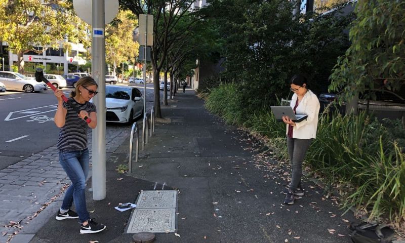 Two researchers conducting the experiment. One of them is hitting the pavement with a sledgehammer while the other stands nearby watching the incoming data on a laptop.
