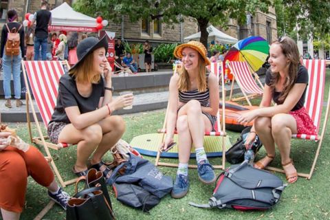 Three women sit on deck chairs and laugh together on campus.