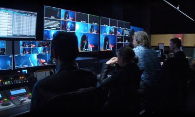 Four people in a dark room sitting behind monitors watching a live performance