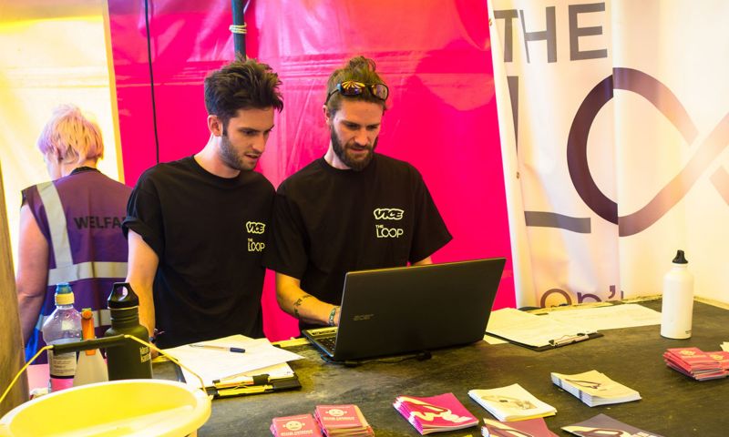 Two men look at a laptop computer at a drug checking booth.