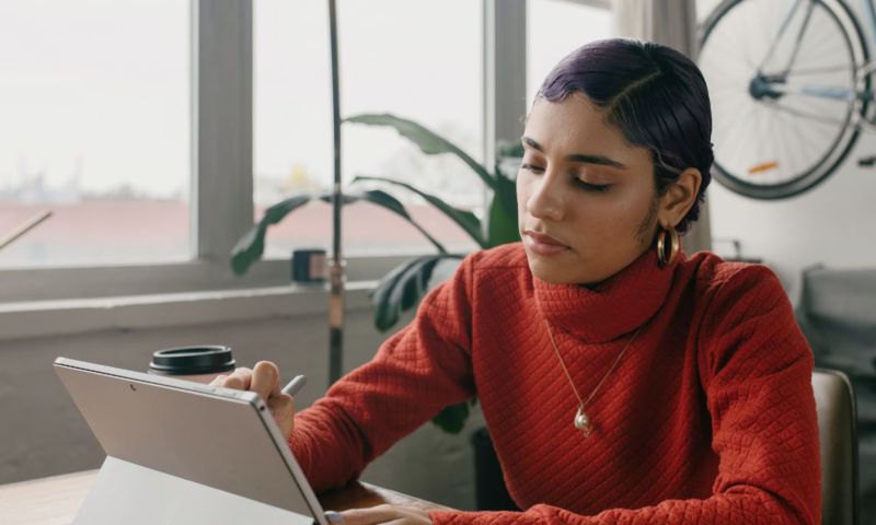 A woman in a red sweater works on a tablet computer.