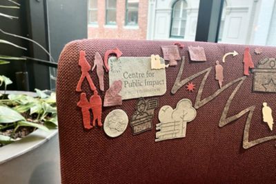 Felt cutouts of people and shapes are displayed on the back of a chair. There is a plant next to the chair
