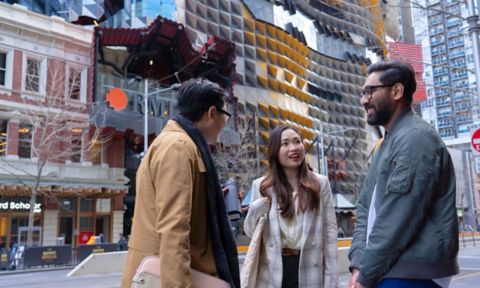 Three RMIT students standing in front of RMIT builds with colourful architecture