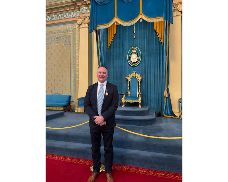 Dr Paul Kremer standing on red carpet in front of an ornate gold chair on a raised platform with a rich blue curtain as a backdrop.