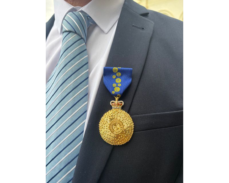 Close up of an Order of Australia medal pinned to a person wearing a grey suit and a light blue striped tie