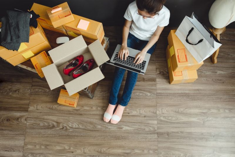 Woman typing on laptop while sititng next to delivery boxes