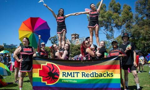 Redback cheerleaders holding up two of their squad with a rainbow pride banner in front of them,