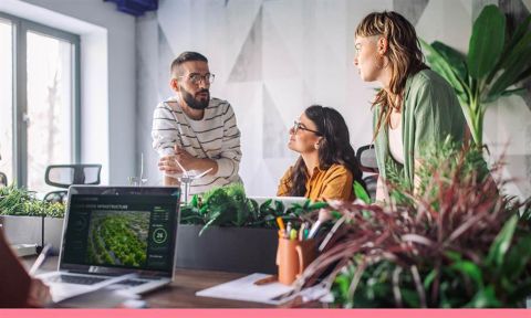A men and two women work collaboratively at a desk.