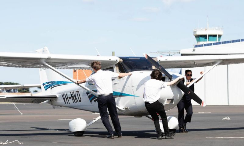three pilots standing with a small plane on tarmac