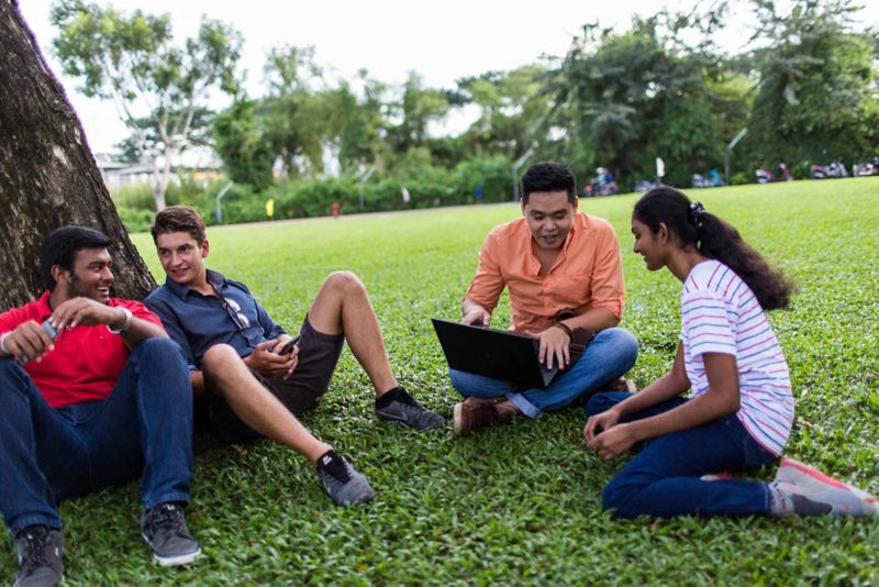 A group of international students discussing while sitting on the grass