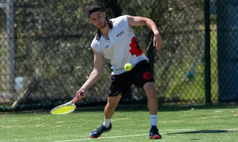 A tennis player wearing a redbacks uniform is just about to hit the ball with their racket