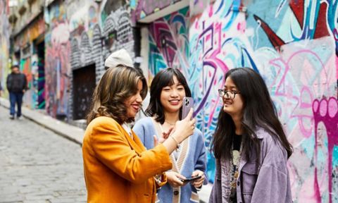 Three students smiling while looking at a smartphone in Melbourne.