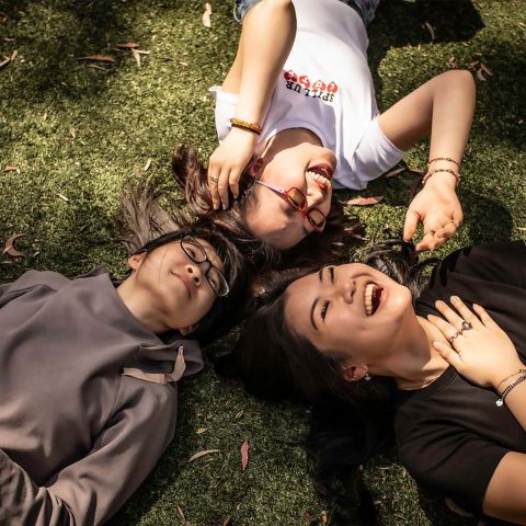 Three female international students laying on the grass smiling and laughing