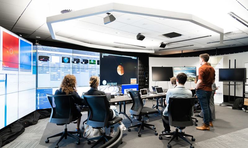 Post-graduate students working around a table with large displays on the wall.