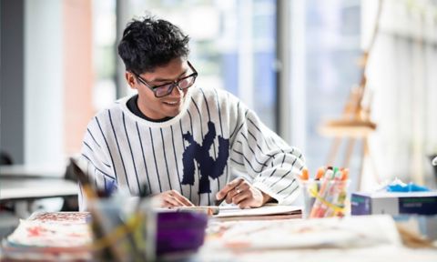 Student smiling, reading a book in an art class.