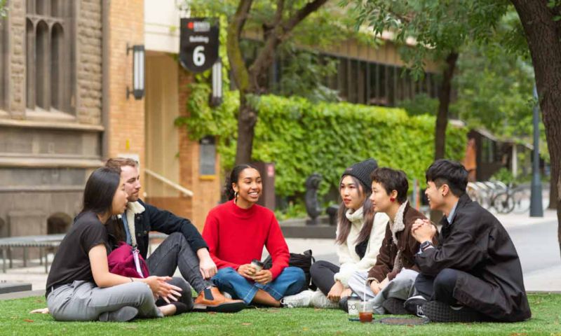 A group of students sitting on grass, smiling and chatting