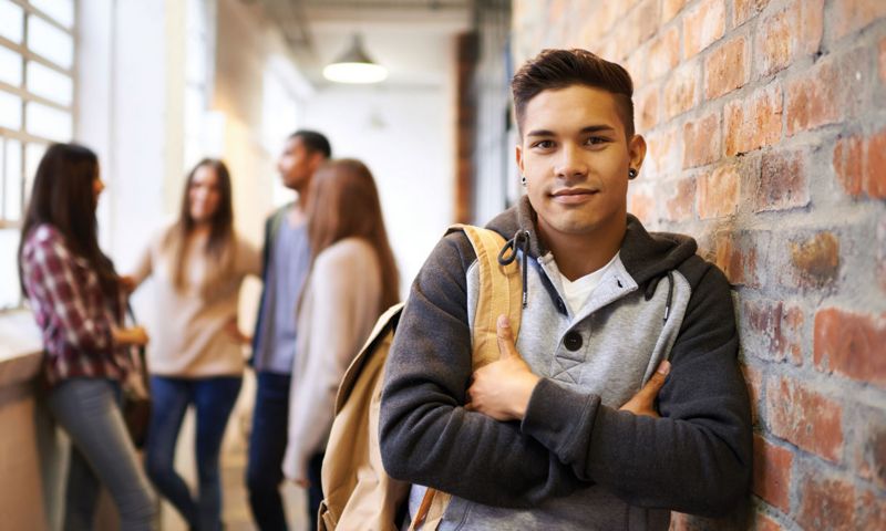 Student smiling and leaning against a brick wall