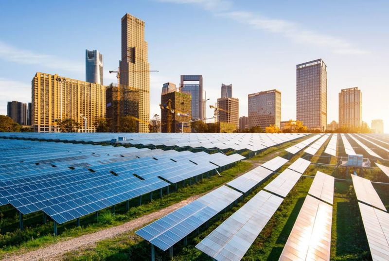 A landscape view of a solar panel field with buildings behind