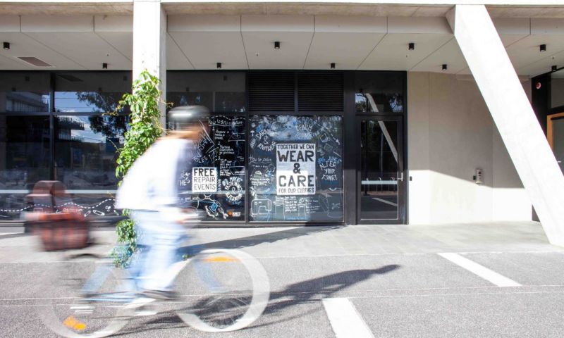 A person on a bike wearing a helmet rides past a building with a sign in the window advertising free clothing repair events