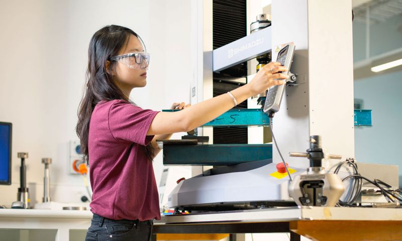 A woman uses a machine and wears safety glasses.