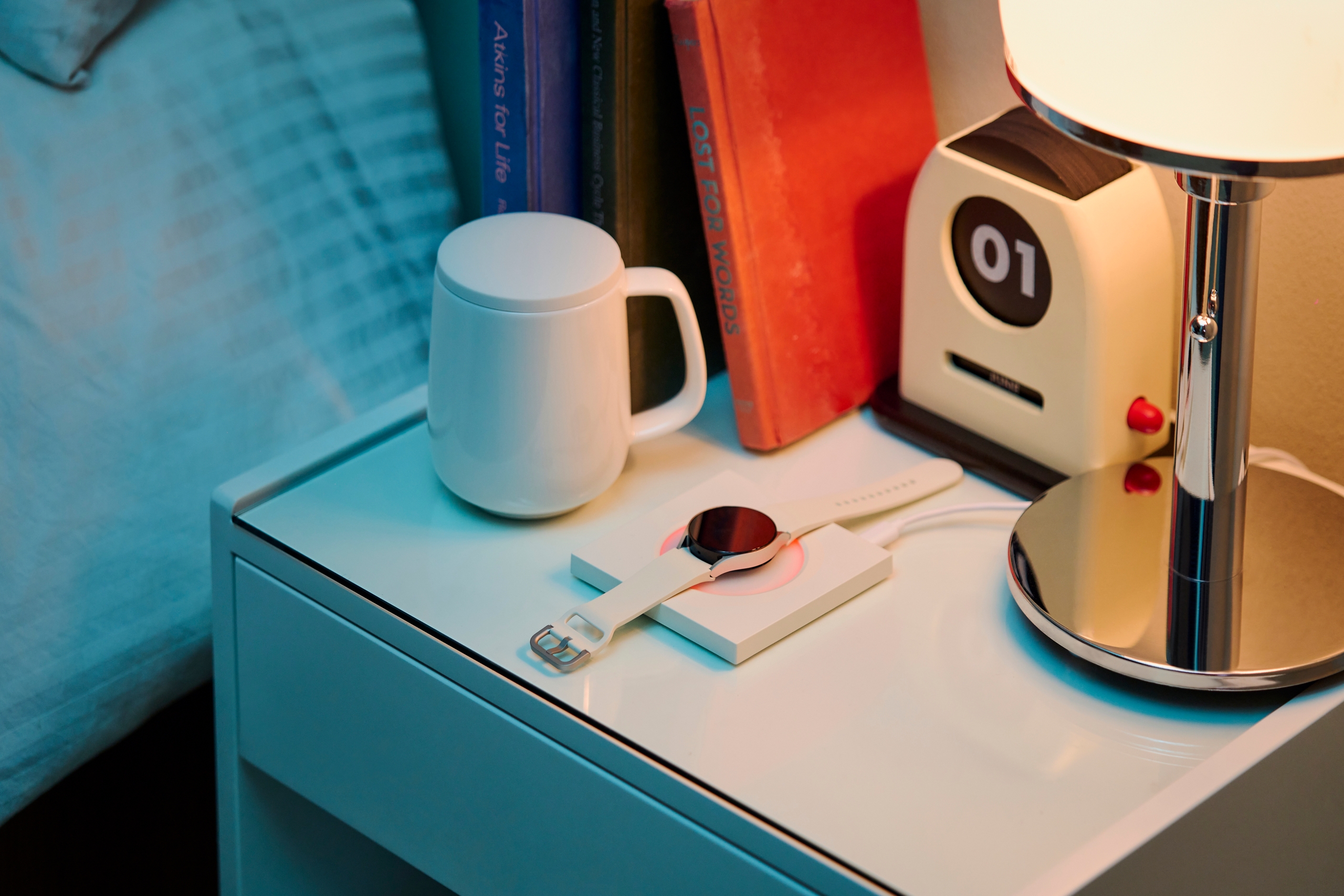 Smartwatch charging on pad beside a ceramic mug.
