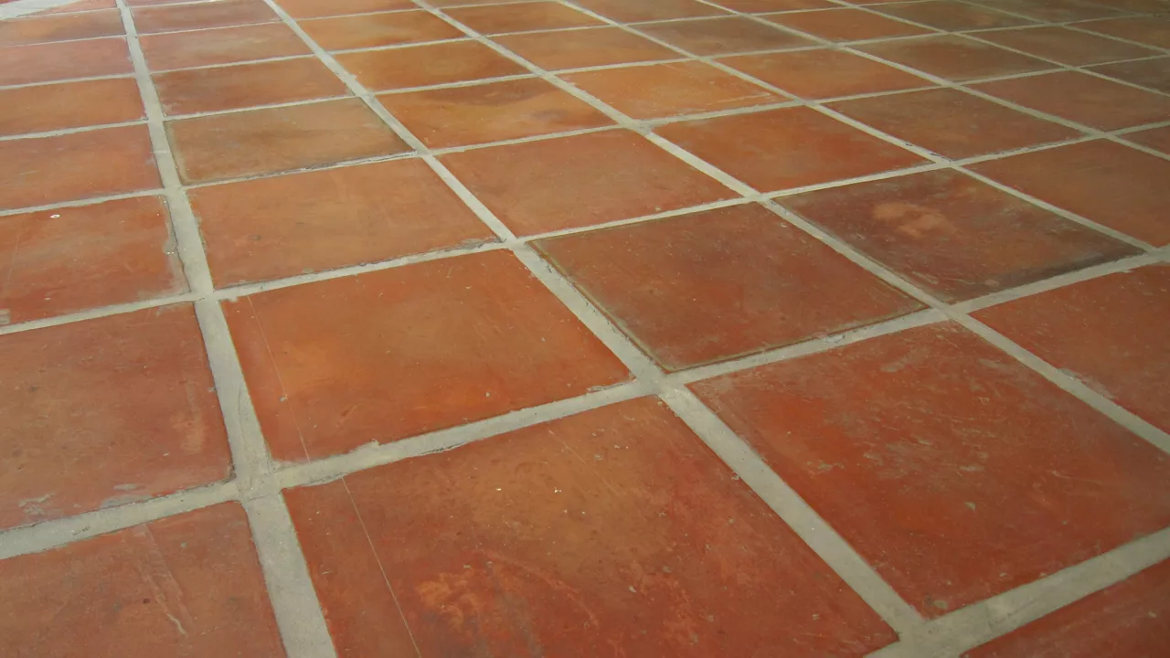 A floor of square terracotta tiles in a grid arrangement, showcasing warm, reddish-brown hues, signs of wear, aging and light grey grouting,plat brick