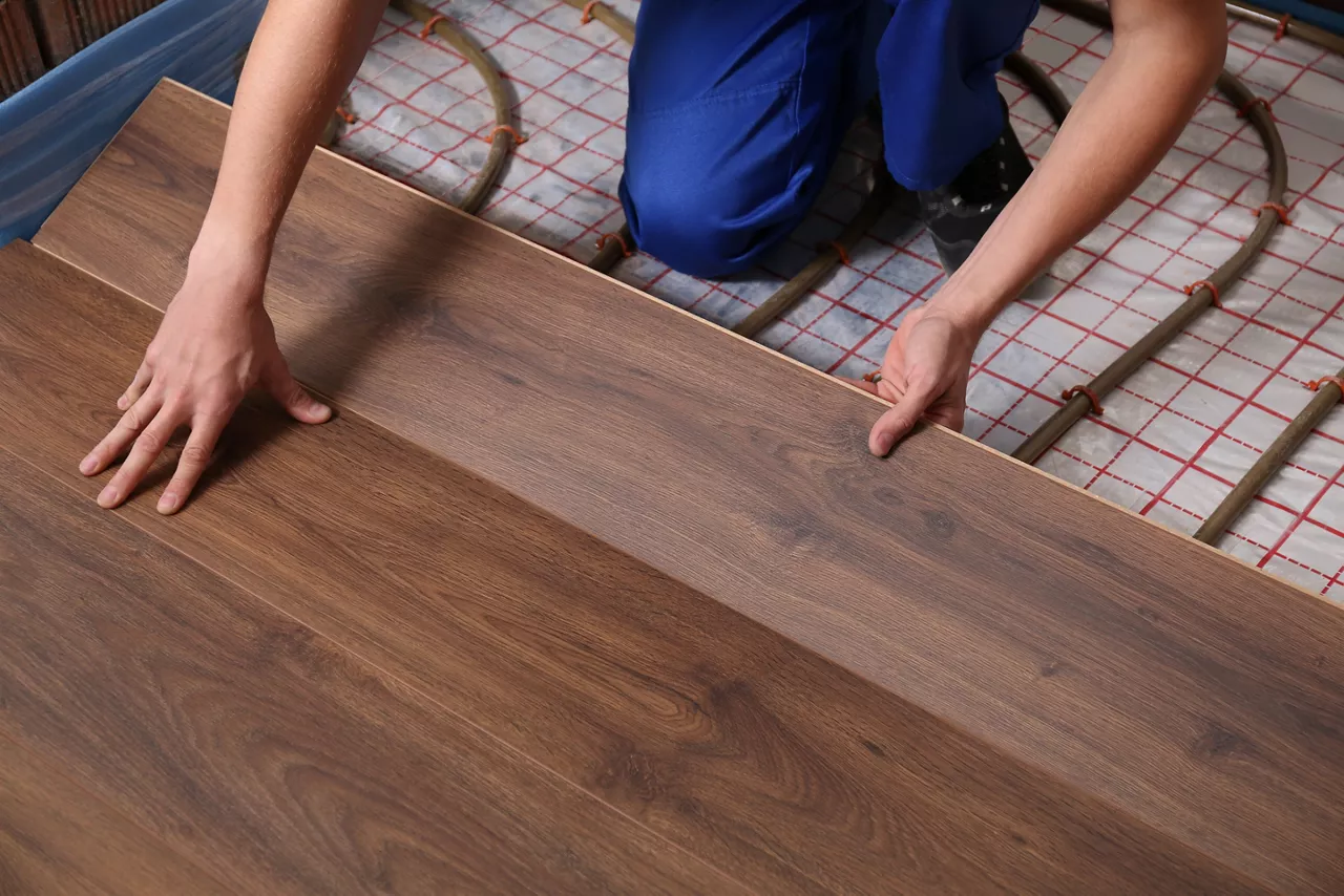 Worker installing new wooden laminate over underfloor heating system, closeup