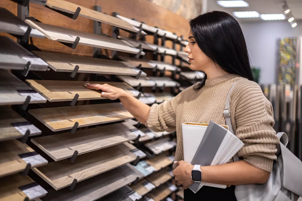 Happy brunette female interior designer choosing flooring tile color texture samples at store shop. Woman architect choice floor and wall finishing material for architecture and construction industry
