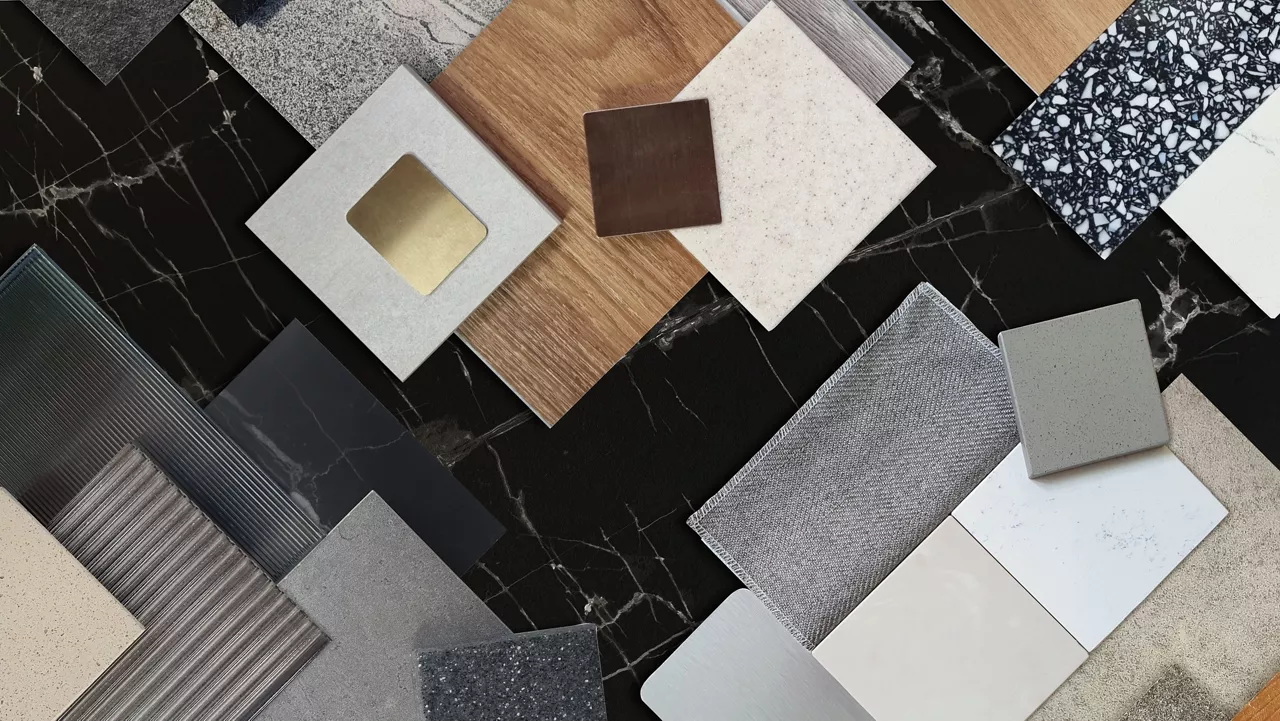 interior material samples contains panels and tiles. interior moodboard including terrazzo, quartz, stone tiles, blue laminated, wooden flooring tiles, gold stainless placed on black marble table.