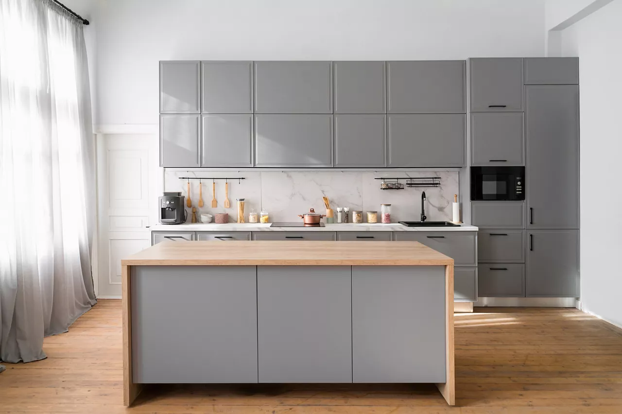 Bright minimalistic kitchen interior with gray furniture and big dining table on wooden floor. Cooking utensils and jars with food on countertop.