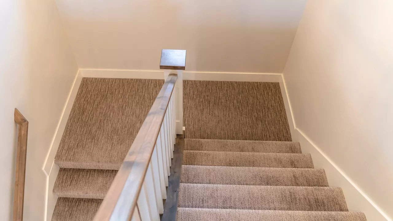 Photo Panorama U shaped staircase with handrails and gray carpet inside a home with white wall