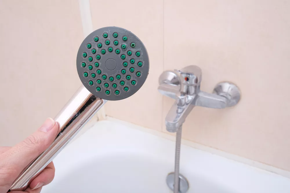 A hand holding shower head in bathroom, water tap on background, cleaning of clogged nozzles.