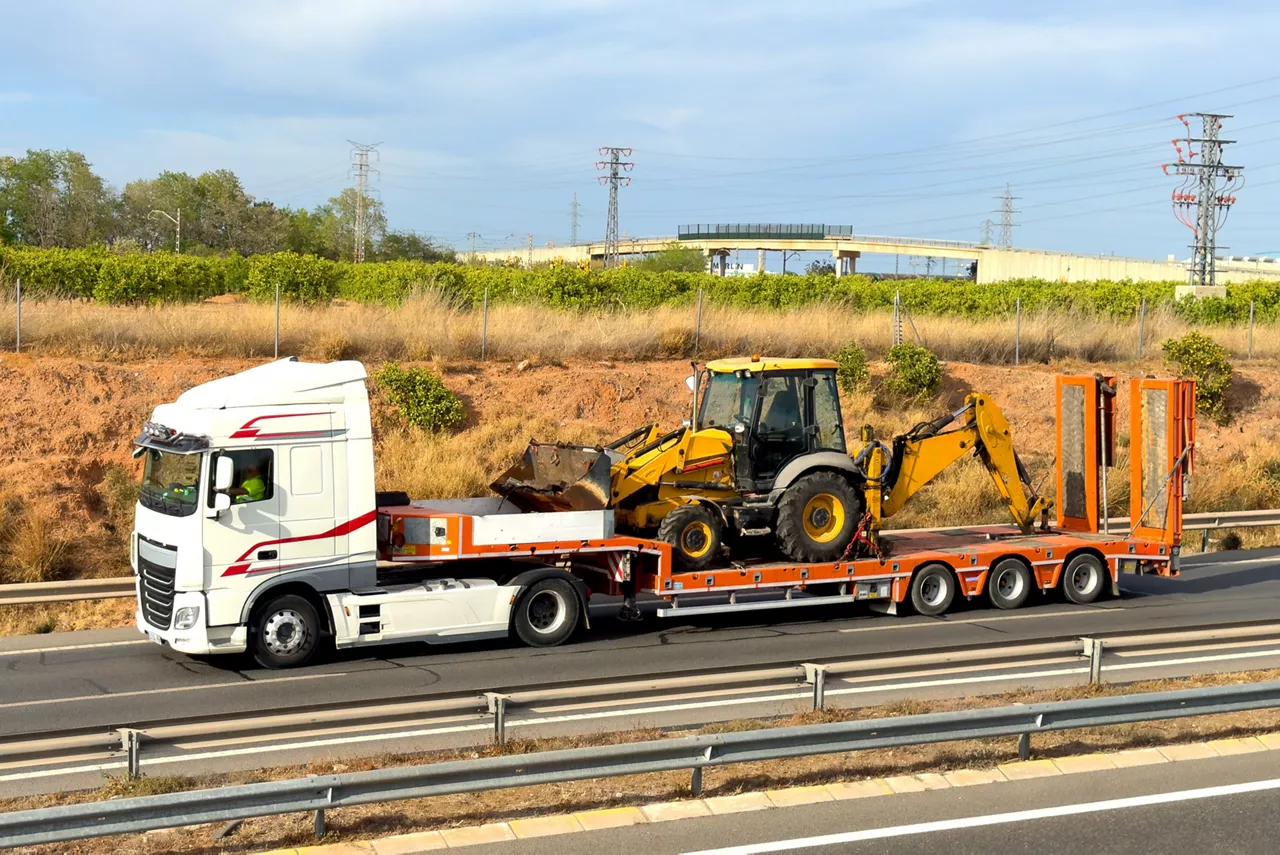 Transportation of Construction tractor. Semi truck transporting a tractor on road. Transport, Shipping, hauling. Heavy duty tractor unit with push-pull. Transportation of heavy and oversized cargo.