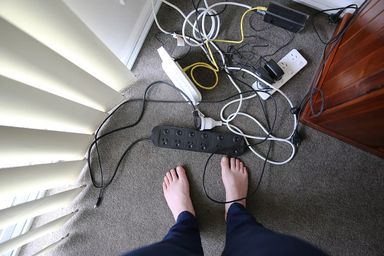 A woman stands in front of a tangled mess of electrical cords and plugs 