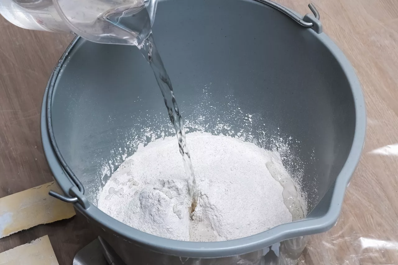 Mixing white plaster in a bucket with a stirrer. Close-up.