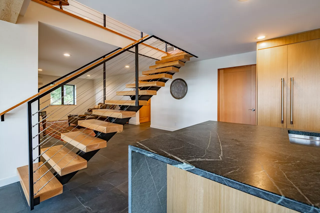 Modern open concept home interior kitchen with floating stairs and grey slate floors beamed ceiling and wood cabinets