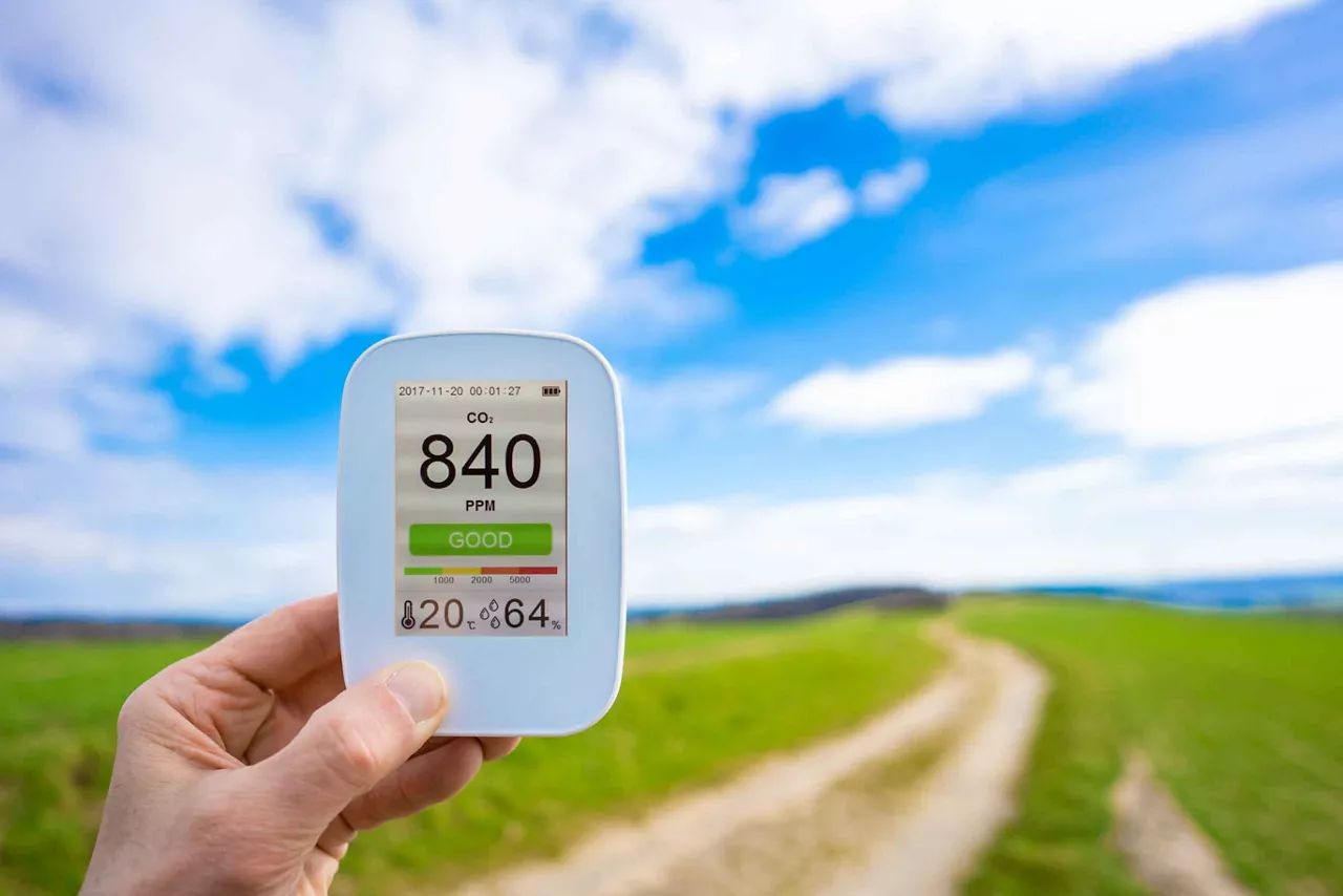 air quality monitor in the hand against the background of a green summer field shows the CO2 content