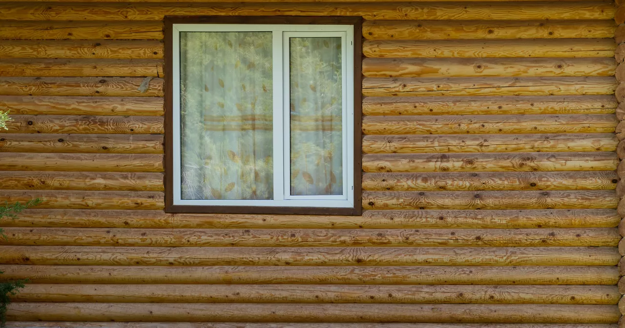 White window in a wooden wall of a house made of pine logs. Modern plastic uPVC window.
