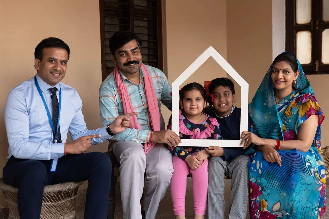 Happy rural indian family forming house roof with their hands at village home, Parents care for child protection, Rural family sitting with insurance agent. Concept of home loan and Insurance Concept.