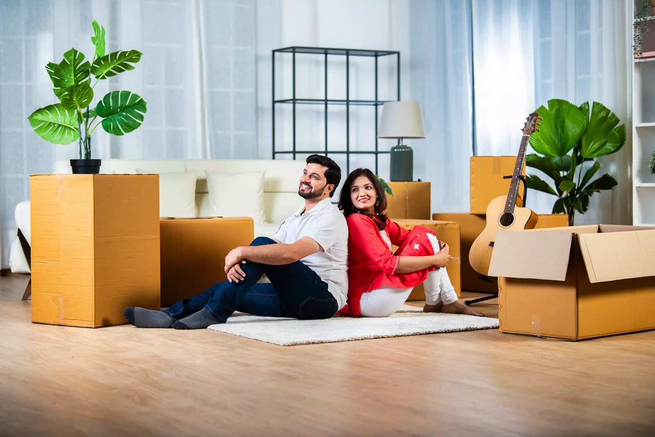 Home moving concept, Indian young couple sitting on floor of living room with cardboard boxes