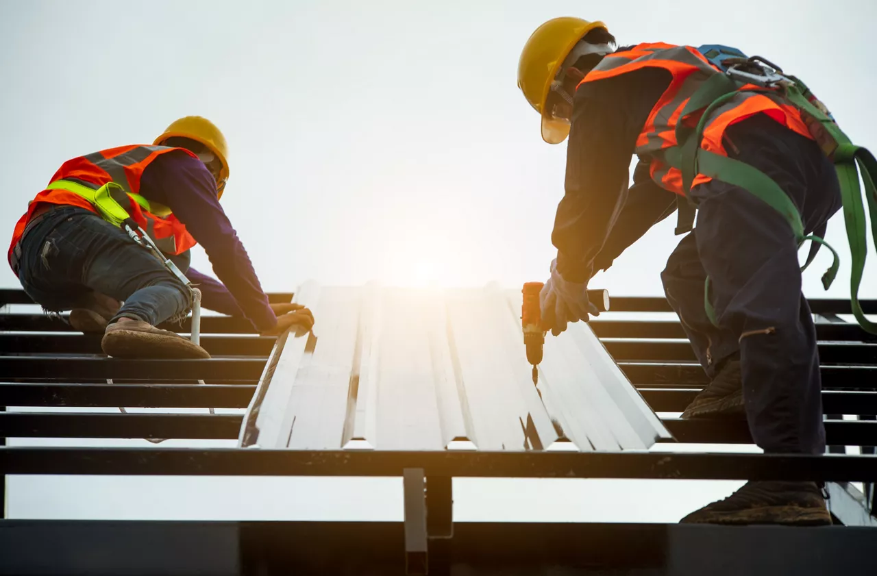 Construction engineer wear safety uniform using an electric drill and screw tools to fasten down metal roofing work for roof industrial concept with copy space