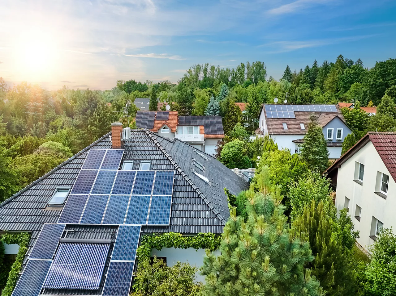Aerial view of the roofs of houses covered with solar panels. Family houses in gardens, photovoltaic panels on the roof, summer, blue sky with white clouds. Home Electricity Generation, green living.
