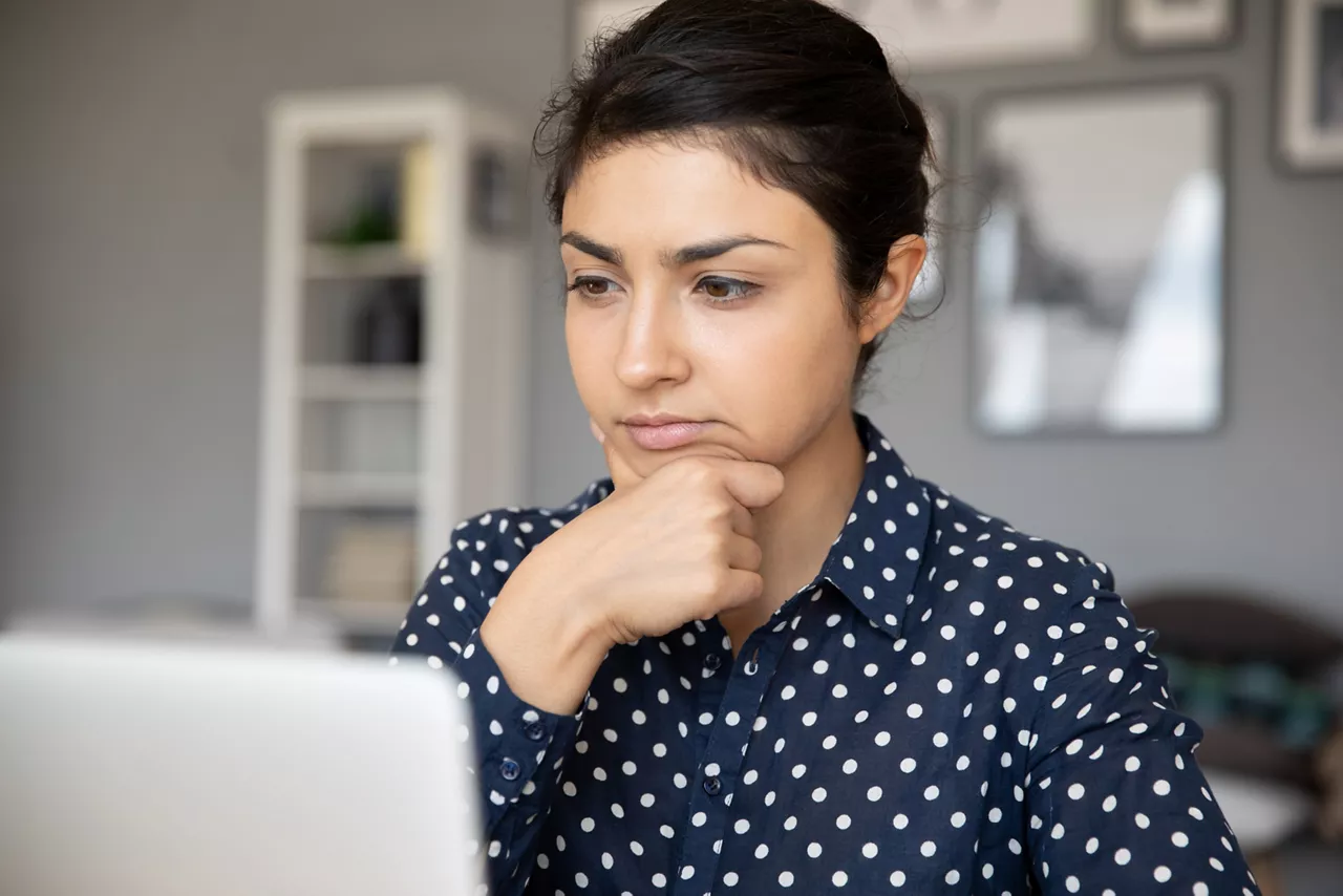Unsure Indian business woman sit at desk looks at laptop screen thinking over task do research analyzing results feels doubtful. Concentrated serious office worker cogitating making decision concept