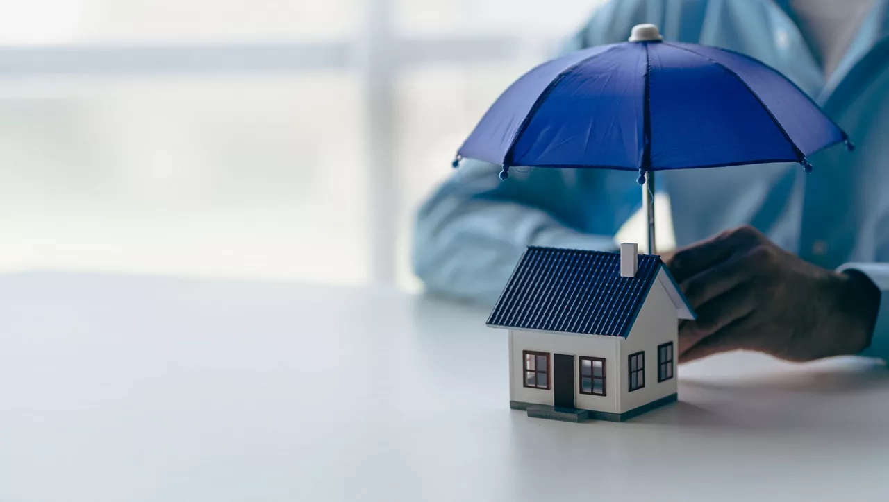 Businessman holding blue umbrella over model of wooden house real estate concept Insurance and property are symbols of housing security.